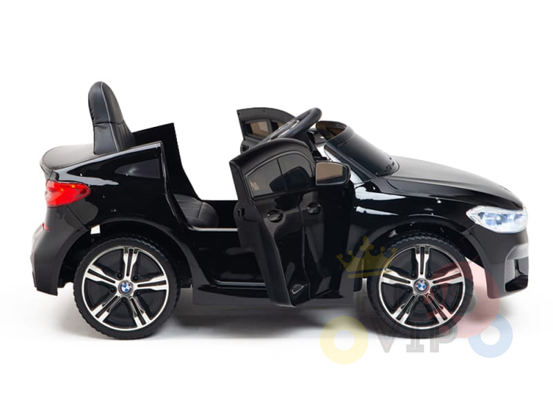 The Black Licensed BMW GT 12V Kids Ride On Power Car features realistic open doors, two seats, a steering wheel, and large wheels. It resembles a luxury vehicle and is positioned against a plain white background.