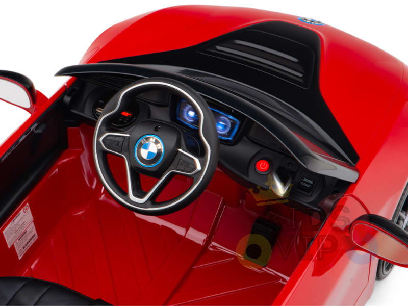 The interior of the Red Licensed Sport BMW I8 12V Kids Ride On Power Car features a black steering wheel with logo, detailed lit dashboard, red plastic seat, and includes a parental remote control for safety.