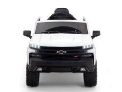 Front view of a white 12V Chevrolet Silverado ride-on truck for kids features upgraded elements like a realistic grille, LED lights, black accents, oversized wheels, and visible steering wheel. It includes music and remote control functionality.