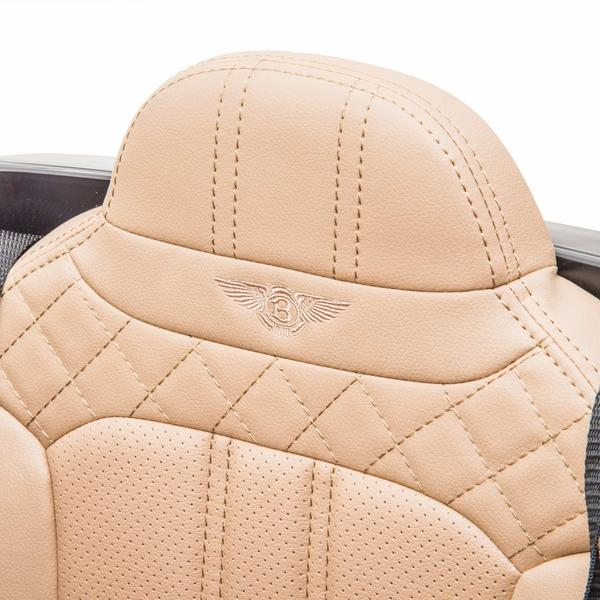 Close-up of a tan leather headrest in a White 12V Bentley Bentayaga Kids Ride On Car, featuring quilted stitching and an embossed Bentley logo with wings around the letter B.