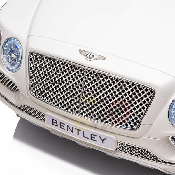 Close-up of the white 12V Bentley Bentayaga Kids Licensed Ride On Car, highlighting the grille with a Bentley emblem. The elegant headlights shine above the BENTLEY license plate. Ideal for stylish playtime, this 1-seater features rubber wheels and a remote.