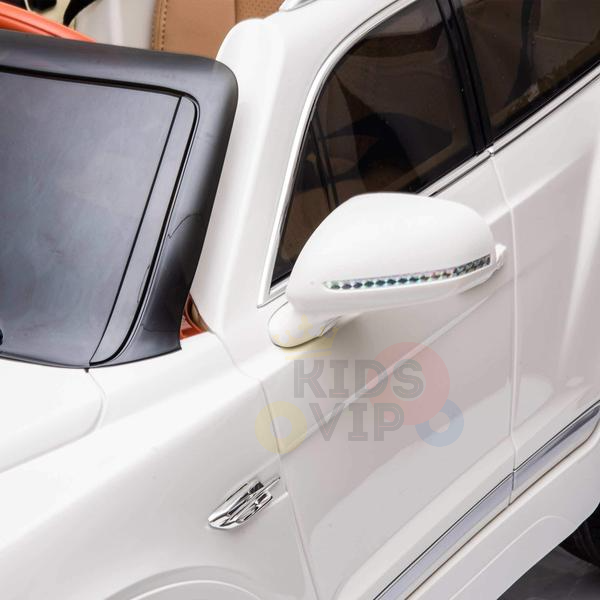 A close-up of the White 12V Bentley Bentayga Kids Licensed Ride On Car showcases its black plastic windshield, side mirrors with LED lights, and a sleek modern design. The tan interior and colorful side text make it perfect for adventurous young drivers.
