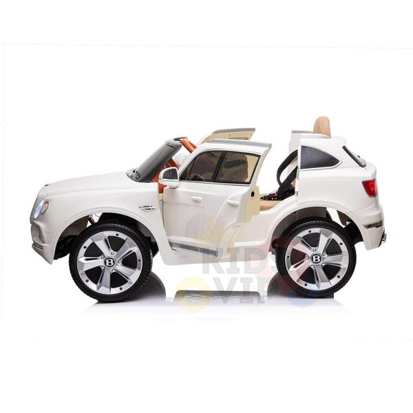 The White 12V Bentley Bentayga Kids Licensed 1 Seater Ride On Car features rubber wheels and open doors revealing a sleek interior, styled like a luxury SUV. Seen from the side on a plain background, it showcases an impressive design. Includes remote control.