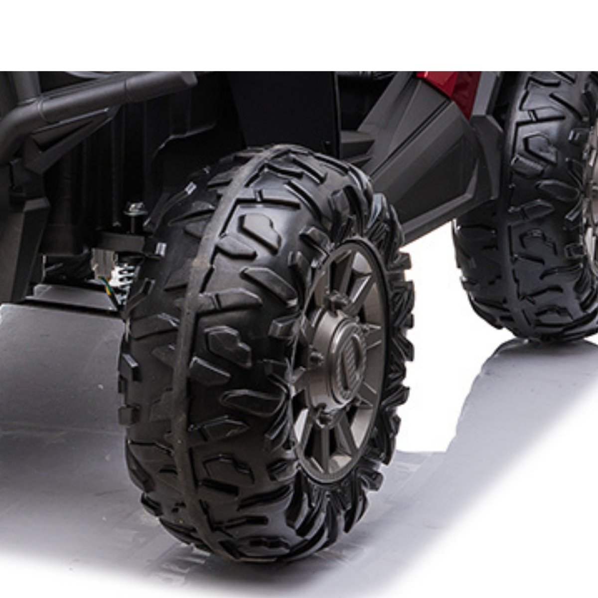 A close-up features rugged black all-terrain tires with deep treads on dark rims. Set on a reflective surface, they are ideal for the Red-Real Paint 2 Seats UTV Adventure Complete Edition 24V Kids Ride On UTV with RC, offering style and durability for young adventurers.