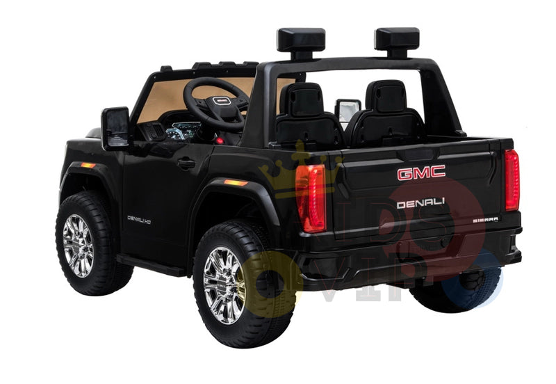 A Black 2x12V Licensed 4WD GMC Sierra Kids Ride On Car with RC, viewed from the rear, flaunts chrome wheels, two rear seats, and a detailed interior with a steering wheel. The model name adorns the back, and it includes a parental remote control for safety.