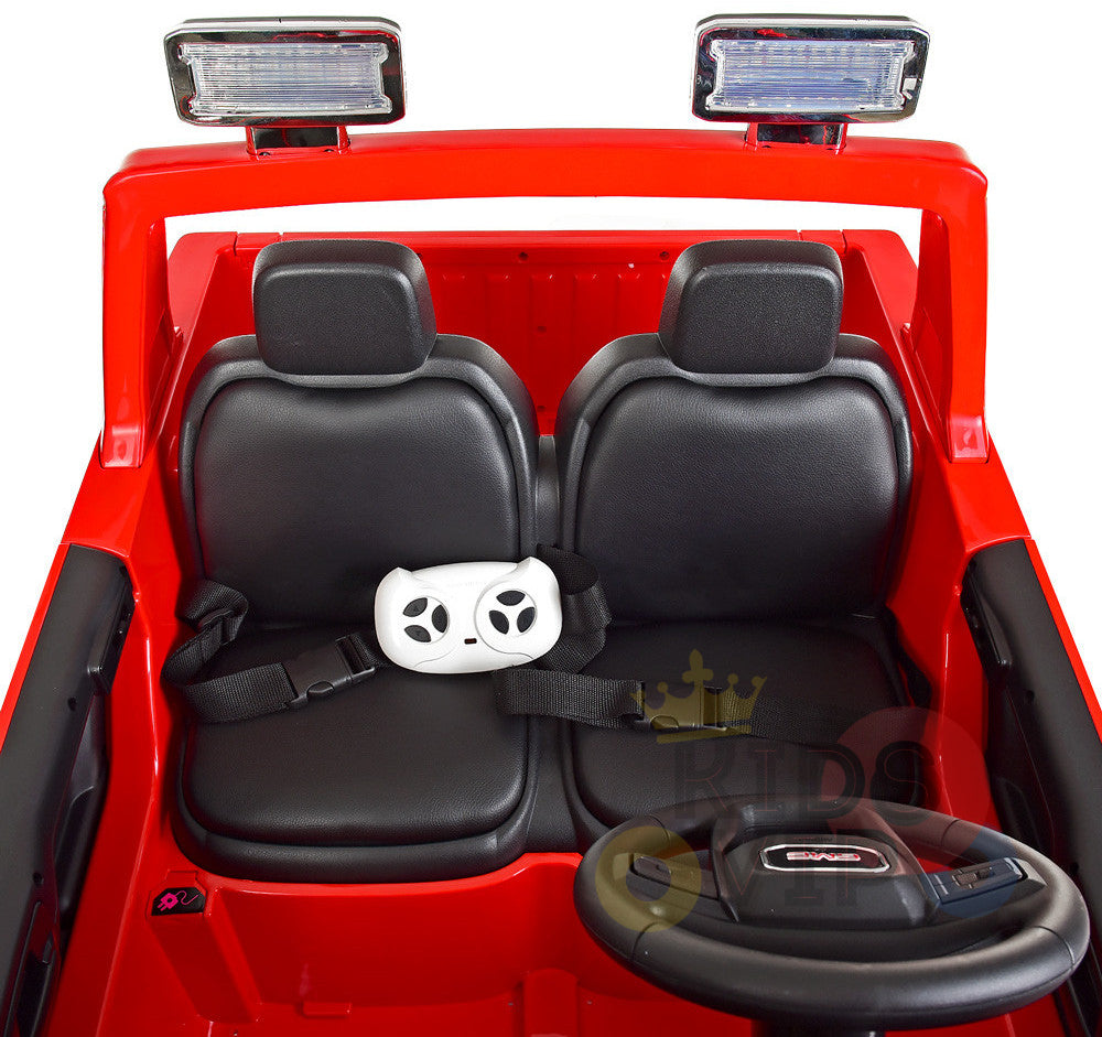 The Black 2x12V Licensed 4WD GMC Sierra Kids Ride On Car features two black seats, a small steering wheel, and a gaming-style remote secured on the left seat with a seatbelt. Above the windshield, it has two rectangular lights mounted on the frame.