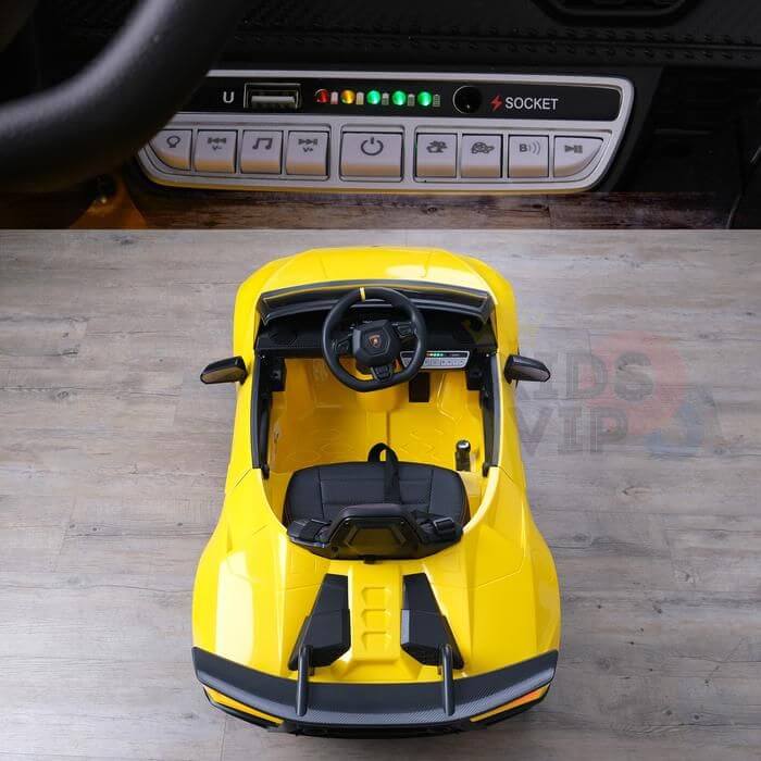Top view of the Yellow Officially Licensed 12V Lamborghini Huracan Sports Edition Ride on Car with a black interior on a wooden floor, featuring a close-up of its remote control panel with buttons, USB port, and LED lights.