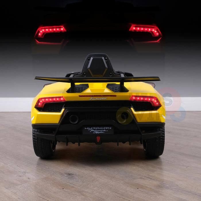A yellow Officially Licensed 12V Lamborghini Huracan Sports Edition Ride on Car is shown from the back on a wooden floor with illuminated LED taillights that reflect and shimmer on a shiny surface in the background.