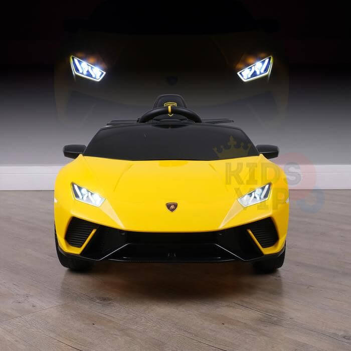A Yellow Officially Licensed 12V Lamborghini Huracan Sports Edition Ride on Car illuminates with its headlights while sitting on a wooden floor. The dark backdrop enhances its brightness, and a remote control is ready nearby for an interactive experience.