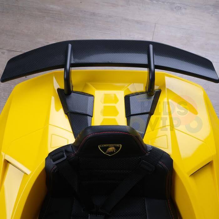 Yellow Officially Licensed 12V Lamborghini Huracan Sports Edition Ride on Car features a black leather racing seat and large rear wing. Its interior and split spoiler design are visible from above on a wooden floor.