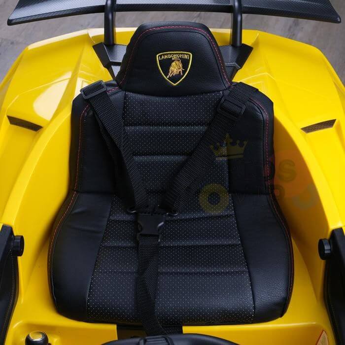 The close-up shows a black leather seat with red stitching and a yellow Lamborghini emblem, fitting the sporty design of the Yellow Officially Licensed 12V Lamborghini Huracan Sports Edition Ride on Car. It features a safety harness within its vibrant yellow body.