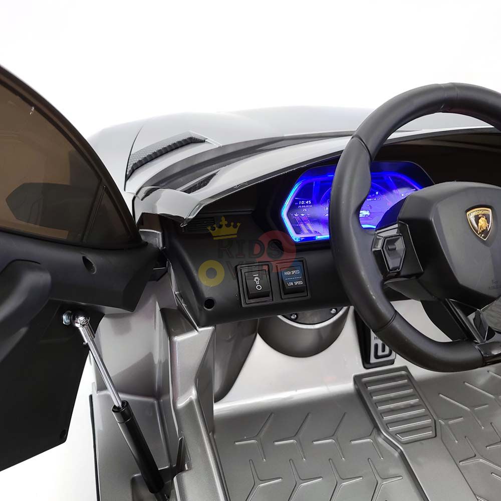 The image displays the interior of the 24V Complete Edition Lamborghini Sport Car. It features a steering wheel, foot pedals, and a blue-lit dashboard. The door is open, showing the seat and floor mat—an exciting choice with KidsVip Warranty included.
