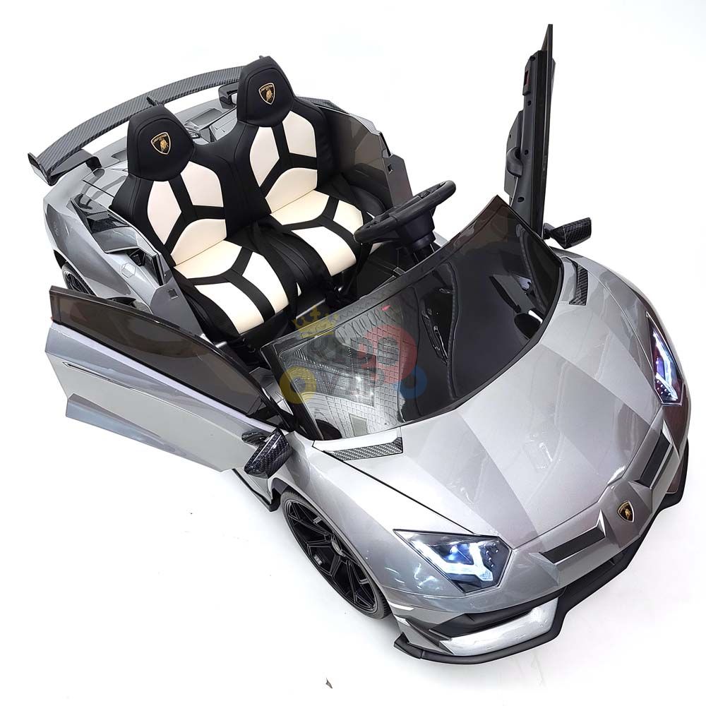 The Complete Edition 24V Lamborghini Sport Car features sleek silver design, open scissor doors, black and white seats, steering wheel, windshield, and illuminated headlights. This toy captures the essence of a drifting sports car with detailed sporty looks. Includes KidsVip Warranty for peace of mind.