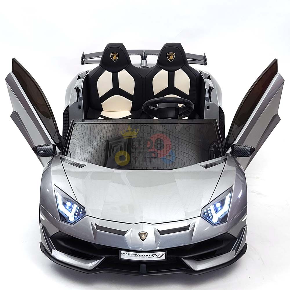 The Upgrade Your Ride: Experience the Thrill of Drifting with the Complete Edition 24V Lamborghini Sport Car is a silver toy car with open scissor doors, black seats, detailed steering wheel graphics, brilliant headlights, and a small crown on its windshield, set against a white background.