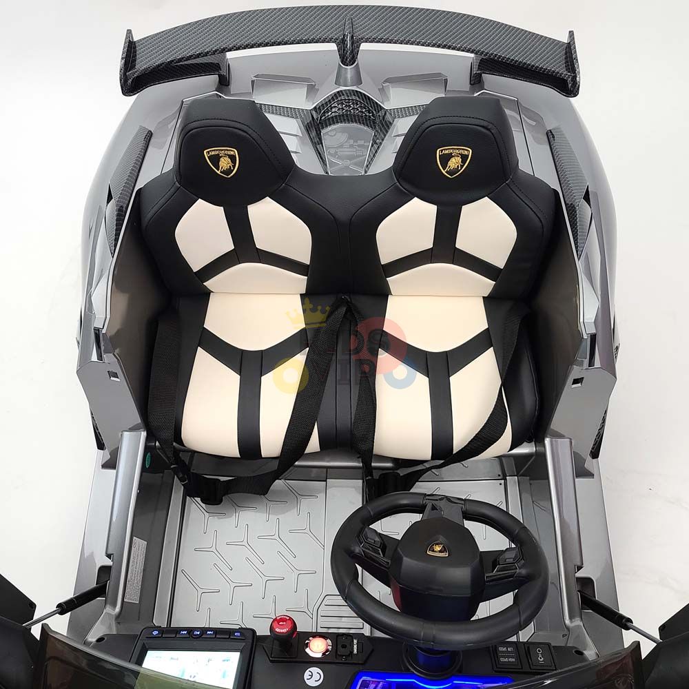 Top view of the Complete Edition 24V Lamborghini Sport Car, boasting luxurious black and beige seats with harness straps, steering wheel, dashboard controls, and patterned floor mats for thrilling drifting fun. Enjoy peace of mind with KidsVip warranty.