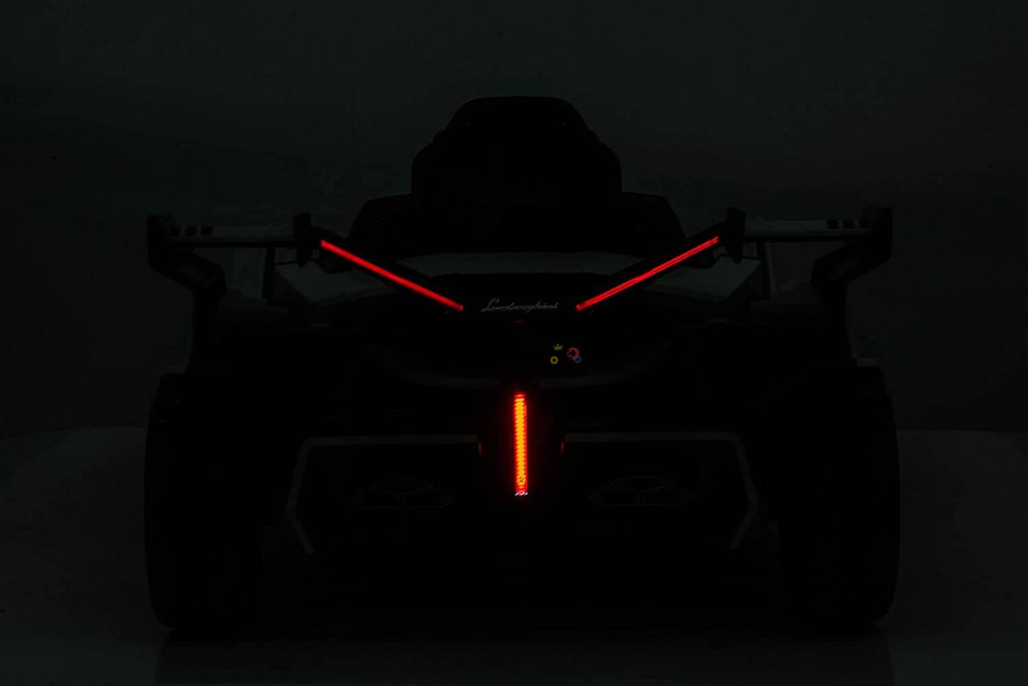 The Pink 12V Official Lamborghini Vision GT Kids Ride-on Car features a sleek, angular design with prominent red LED lights forming an X shape at the front, exuding a modern vibe against a dark background, reminiscent of its futuristic inspiration.