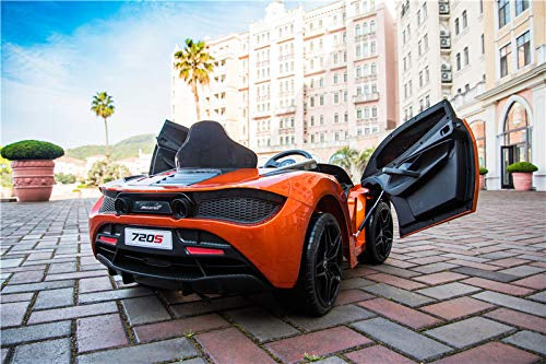 The Orange 12V McLaren 720S Kids Licensed 1 Seater Ride On Car with Rubber Wheels sits on a brick path with its doors open, framed by palm trees and a grand building under the clear blue sky—perfect for remote control adventures.