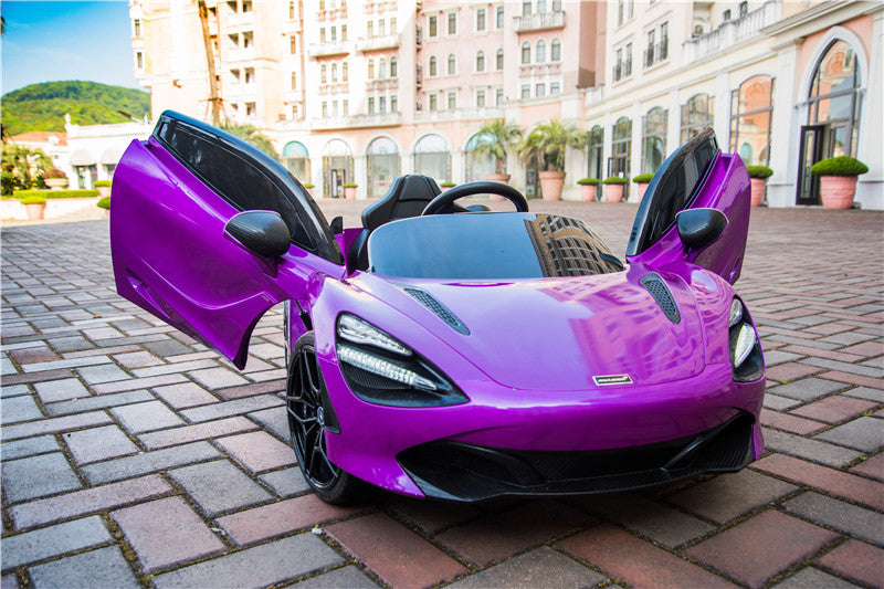 A Purple 12V McLaren 720S Kids Licensed 1 Seater Ride On Car with Rubber Wheels and Remote is parked with its doors open on cobblestones. The backdrop showcases a European-style building with arches and balconies amidst lush greenery.