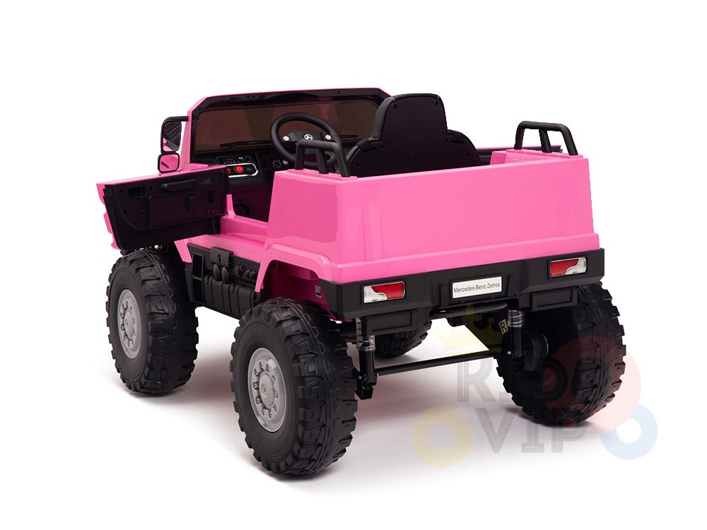 A bright pink 12V Mercedes Benz Zetros Kids 1 Seater Ride On Truck with rubber wheels and remote is pictured. It has doors open, revealing a black interior. Positioned at an angle, it showcases both the back and one side.