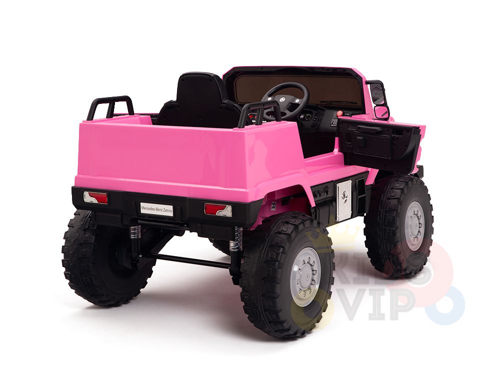 The Pink 12V Mercedes Benz Zetros Kids 1 Seater Ride On Truck with Rubber Wheels and Remote is shown from the back at an angle, featuring large black tires, a sleek black interior with a steering wheel, and an open drivers side door against a white backdrop.
