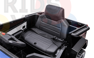 The image shows a close-up of the black leather seat in the Futuristic 12V Fire Truck Ride-On toy for kids and toddlers, surrounded by a steering wheel and textured details. Perfect for remote control adventures, faded colorful letters add to the excitement in the background.