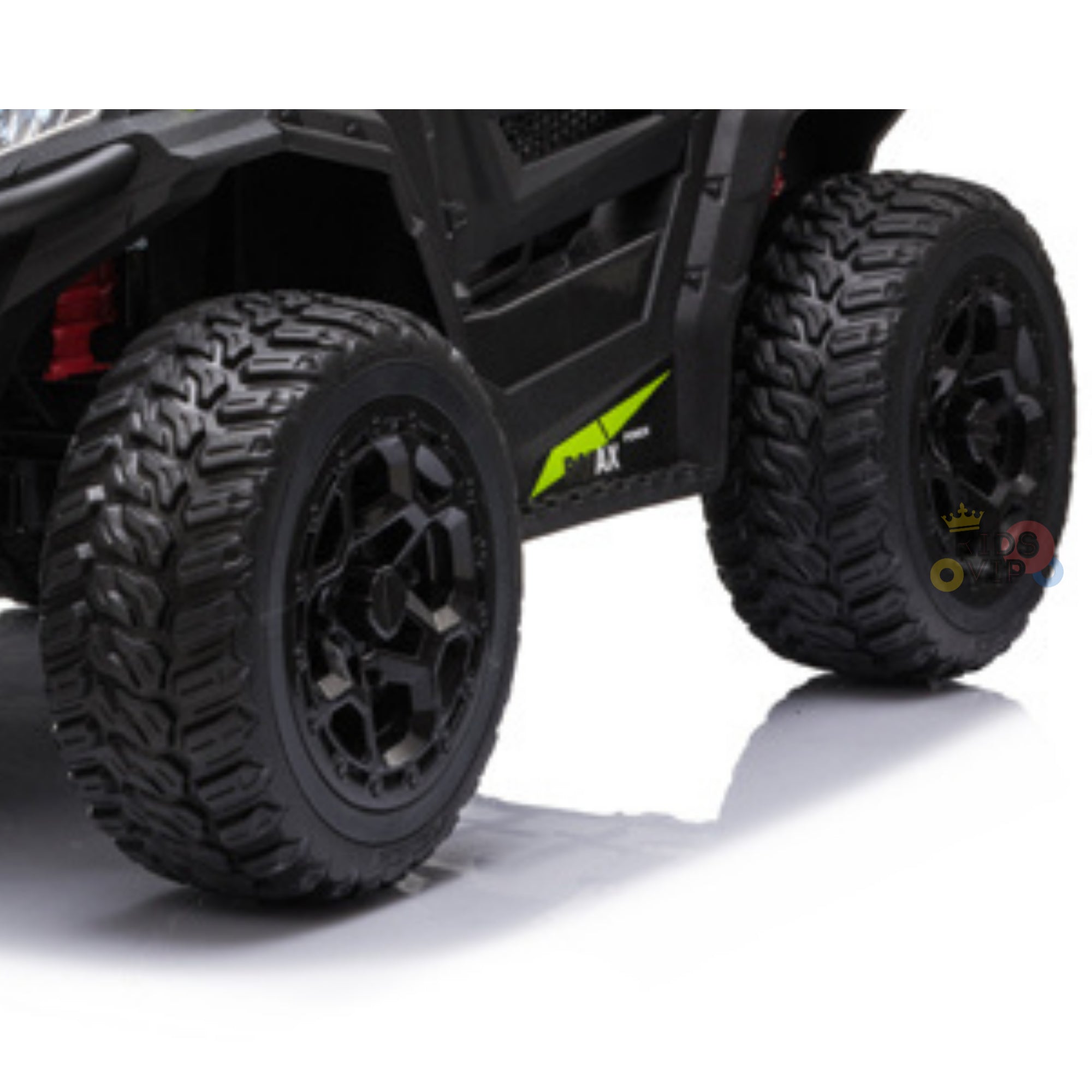 Close-up of the front wheels of the black Upgraded 12V Junior Sport Utility Ride On Buggy/UTV 4WD Edition reveals rugged treads and black rims, complemented by green detailing against a smooth white surface.