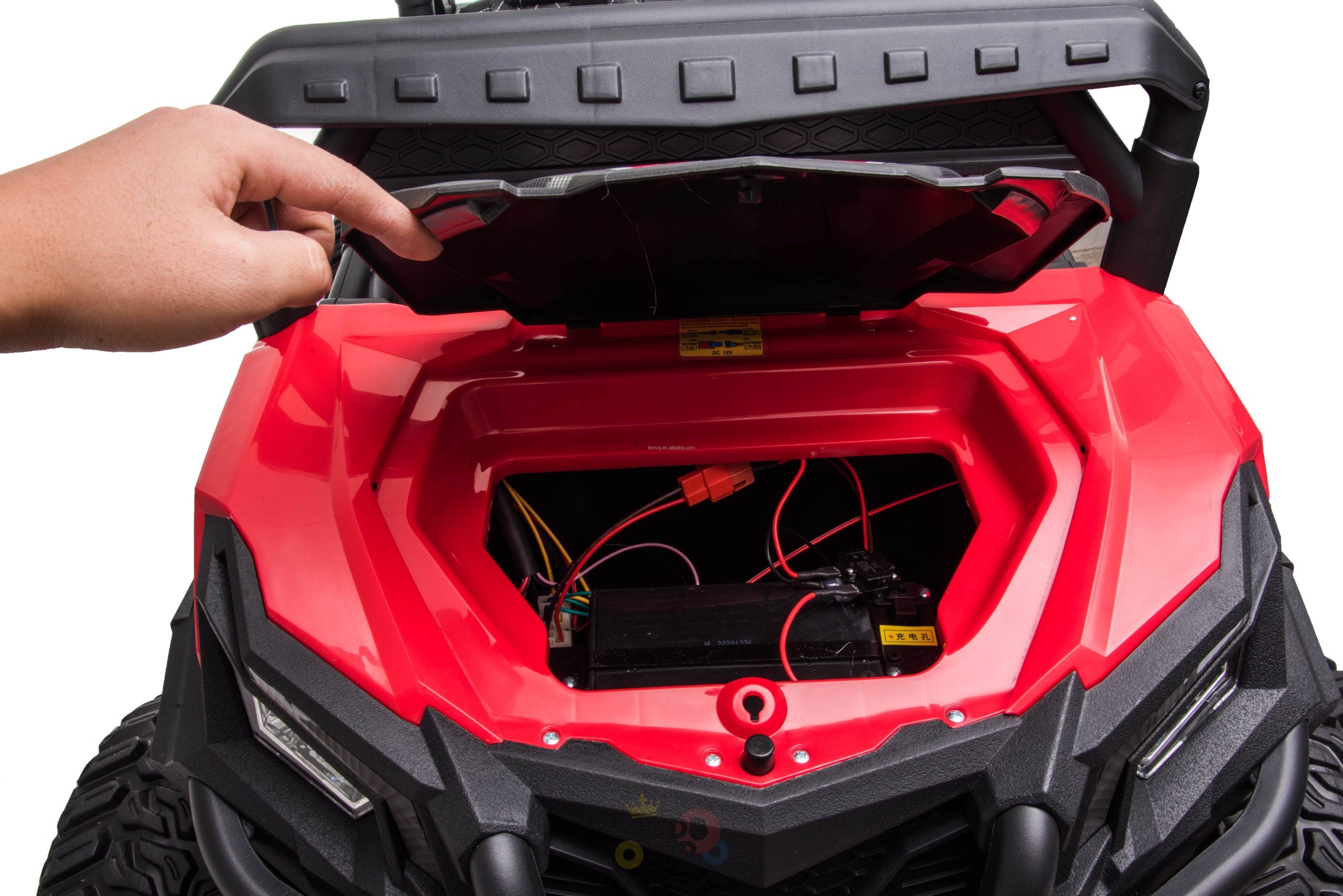 A hand lifts the hood of a red Upgraded 12V Junior Sport Utility Ride On Buggy/UTV 4WD Edition w/Remote Control, revealing internal wires and battery. The vehicle features a black bumper and resembles an off-road ride-on buggy.